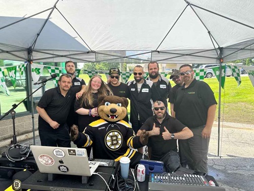 A group of Sullivan Tire employees smiling and happy surrounding Blades, the Boston Bruins' bear mascot.